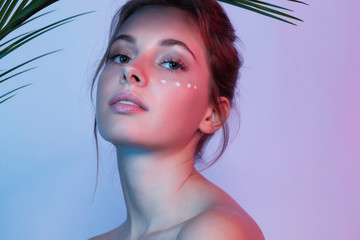 Portrait of beautiful woman looking at camera with calmness. Girl with fresh and clean skin applying wrinkle smoothing cream for skin under eye. Beauty and cosmetics concept. Blurred background