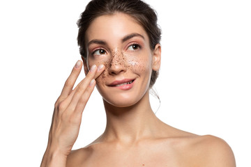 Close up portrait of slyly smiling woman applying cosmetic facial skin scrub, natural coffee mask....