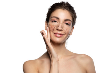 Beautiful smiling naked girl applying coffee scrub, natural peeling mask on face skin. Attractive young woman looking at camera studio portrait. Cosmetology, skincare, therapy. White blank copy space