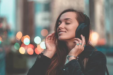  Young happy stylish trendy casual hipster woman teenager listening to music on a wireless headphone while walking around the city. Music lover enjoying music © Goffkein