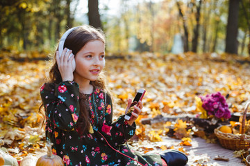 Portrait of a little girl listening to music in headphones in the autumn season.