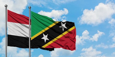 Yemen and Saint Kitts And Nevis flag waving in the wind against white cloudy blue sky together....