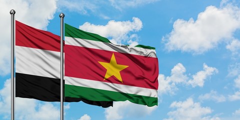 Yemen and Suriname flag waving in the wind against white cloudy blue sky together. Diplomacy...