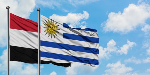 Yemen and Uruguay flag waving in the wind against white cloudy blue sky together. Diplomacy...