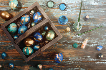 Painted colored Easter eggs in dark wooden box on dark wooden background. Boho stile.