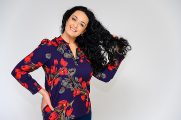 Portrait of a pretty brunette woman with long curly hair on a white background in a color blouse. He stands in front of the camera, smiles, talks in various poses with emotions.