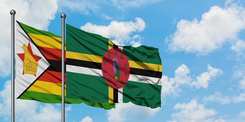 Zimbabwe and Dominica flag waving in the wind against white cloudy blue sky together. Diplomacy...