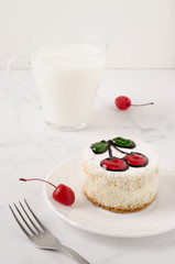 White cherry cake, with decorative cherries, on a plate. There's a napkin next to it. White...