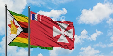Zimbabwe and Wallis And Futuna flag waving in the wind against white cloudy blue sky together....