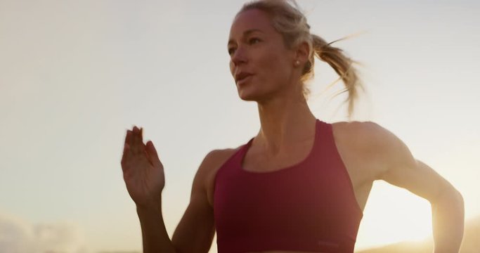 Fit attractive woman running at sunset with golden light, amazing sunset workout in the mountains, determined runner training at sunset achieving her sports fitness goals
