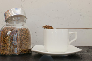 A glass jar of instant coffee in large granules next to a white mug.