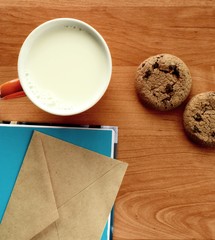 on an alder-colored table is a cup with milk, cookies and a book with an envelope