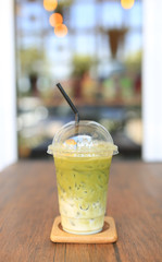Iced matcha green tea latte with milk with brown straw in take away cup on wooden table at cafe.