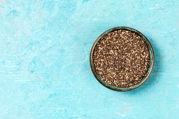 Chia seeds in a bowl, overhead shot on a blue background with copyspace