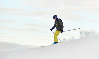 Young sportsman in helmet and goggles enjoying process of skiing on winter vacation. Male skier on slope in mountains. Recreational outdoors concept. Side view. White monochrome. Copy space for banner