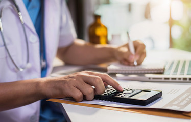 Doctor physician with stethoscope calculate medical fee costs & revenue. practitioner use calculator at Clinic.