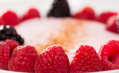 raspberries and blackberries laid out on a white plate in circle with yogurt and cinnamon