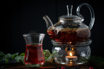 A glass of herbal tea with blackcurrants in a teapot on a dark wooden background. Fragrant natural drink from wild berries.