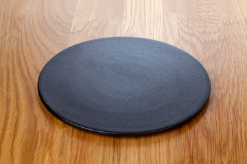 Empty black plate on wooden table.