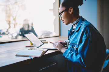 Side view of positive female student using public internet for making shopping on web store during...
