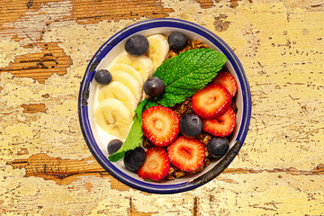 Bowl with granola and fruits on a old wooden table.