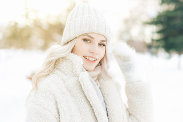 Portrait of a young blonde woman in winter outdoors. Beautiful model girl dressed in light warm clothes looking at the camera and smiling.
