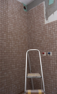 Renovation work performed by the master in the shower room for lining the walls and floors with decorative mosaics using a special tool and white glue for ceramic tiles.
