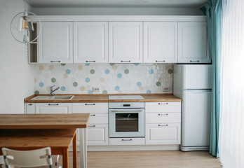 Kitchen interior in white colors with wooden table top and blue mint curtains, classic style. Design idea for small family