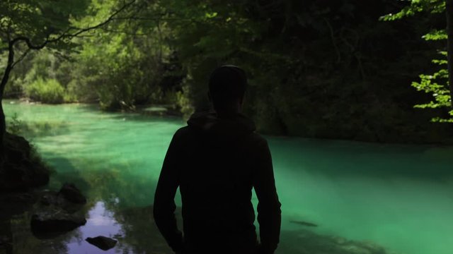Back view man standing in Beautiful background of Turquoise colorful waterfall cascade river lake in Spain in summer. Blue transparent water, and green forest. Pebbles under the water. 4K UHD.