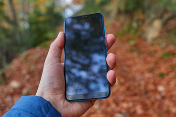 Mobile in someone's left hand, unfocused background with autumnal colors, a path full of brown leaves is intuited