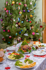 Festive Christmas served table against beautiful green pine tree decorated with many colorful new year toys. Xmas dinner, delicious food, christmas turkey. Winter holidays celebration at cozy home