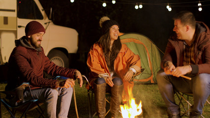 Group of close friend relaxing together around camp fire in a cold night of autumn