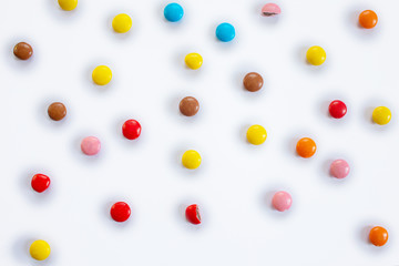 Scattered multi-colored small round candies. Pattern of chocolate dragees in multi-colored glaze on a white background
