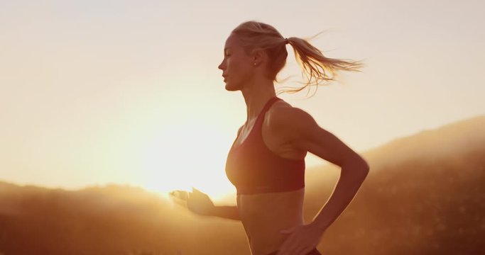 Strong active woman running outdoors at sunset in golden light, mountain running woman training for an ultra marathon