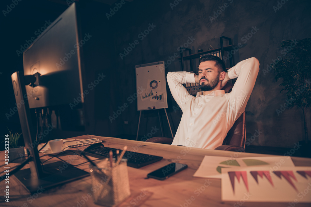 Sticker Portrait of serious boring tired lawyer man sit on chair table look at screen read information dont know what type try finish document company analysis wear white shirt in evening dark office