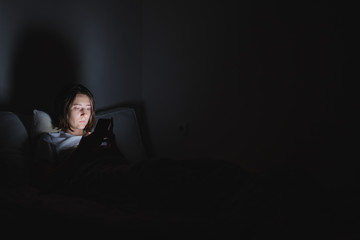 Woman in bed uses phone late at night. Insomnia or excessive usage of social media concept.