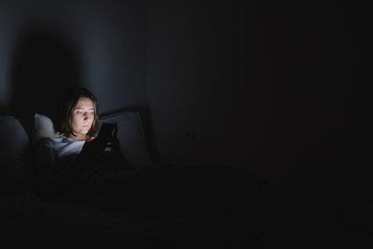 Woman in bed uses phone late at night. Insomnia or excessive usage of social media concept.