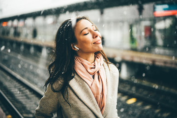 Pretty woman waiting the train at the station. Girl Enjoying winter morning under the snowfall and...