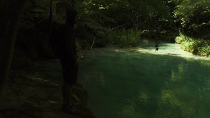 Male Hiker Silhouette taking picture with smartphone of Turquoise colorful waterfall cascade in Spain in summer. Blue transparent water, and green forest. 4K UHD. Hidden Spot. Social media. - Powered by Adobe