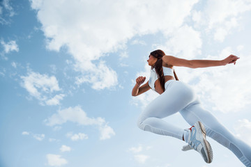Fototapeta na wymiar Up in the sky. Female runner in white sportive clothes doing fitness