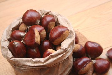 Bunch of ripe chestnuts in a paper bag on wooden background on selective focus