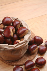 Bunch of ripe chestnuts in a paper bag on wooden background on selective focus