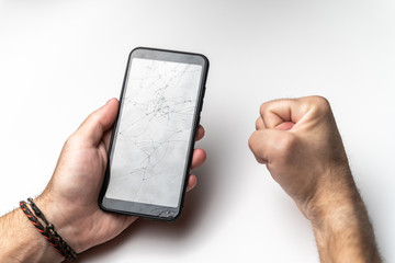 A man's hand and a clenched fist with a mobile phone with a broken screen.