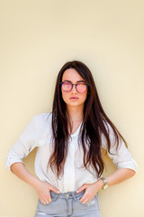 Portrait of a millennial girl with beautiful long shiny hair and mirror sunglasses posing by yellow background and looking at camera.