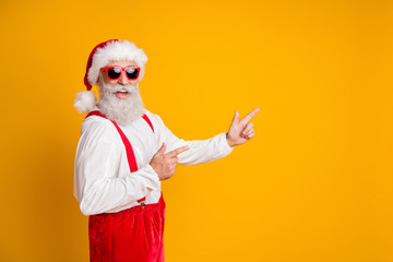 Fototapeta na wymiar 2020 christmas time. Funny funky grandfather in red santa claus hat point index finger copyspace indicate noel tradition x-mas discount wear isolated over yellow color background