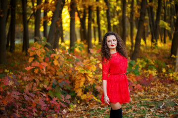 girl with curls in a red dress in the autumn forest