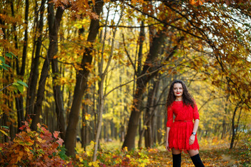 girl with curls in a red dress in the autumn forest