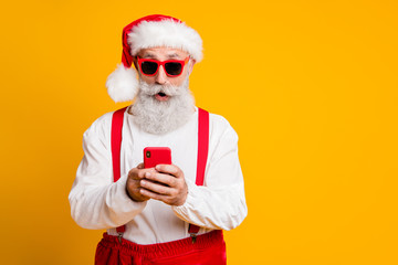 Portrait of funky amazed grey hair santa claus in red hat use smartphone read x-mas shopping...