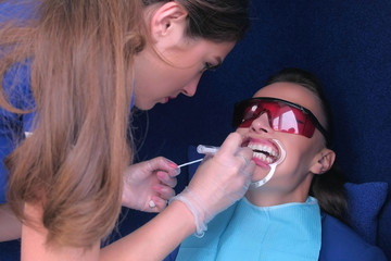 Dentist in sterile gloves applying gel for LED whitening on woman patient's teeth in dentistry....