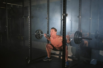 Fototapeta na wymiar Man bodybuilder doing squat exercise with barbell on smith machine at gym. White smoke in gym in dark. Sport motivation. Fit model with perfect body, naked torso, in shorts. Powerlifting concept.